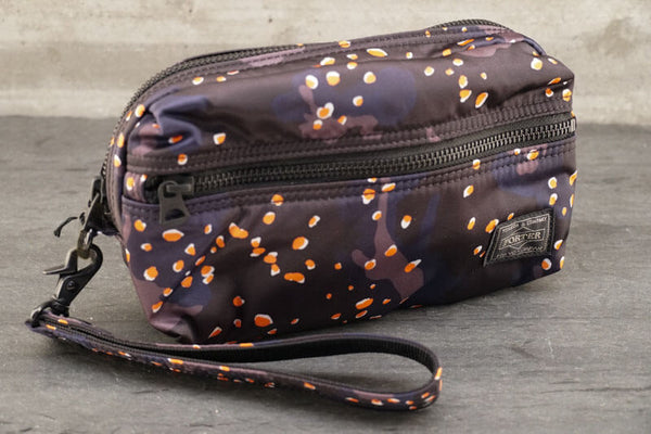 Porter PS Chip Camo Pouch About PS Chip Camo Series The ‘PS Chip Camo’ series is an original PORTER textile design inspired by camo print created for the desert environment in the 1980’s , characterized by the addition of pebbles . The camo print is also unique for its subtle colorway—navy, grey and black— with a pop of orange and white pebbles.